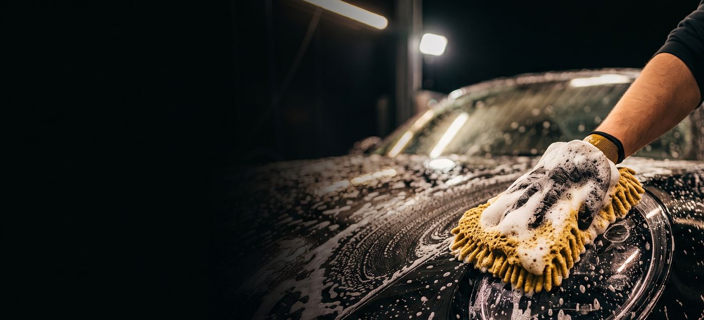 Hand mit Waschhandschuh seift die Motorhaube eines dunklen Autos ein